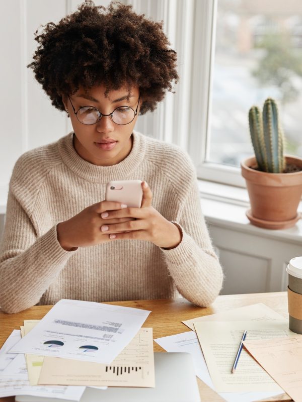 busy-businesswoman-with-afro-hairstyle-works-with-documentation-checks-bank-account-via-cell-phone.jpg